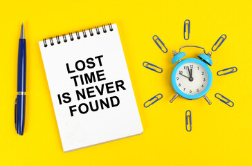 On a yellow surface there is an alarm clock, a pen and a notepad with the inscription - Lost Time is Never Found