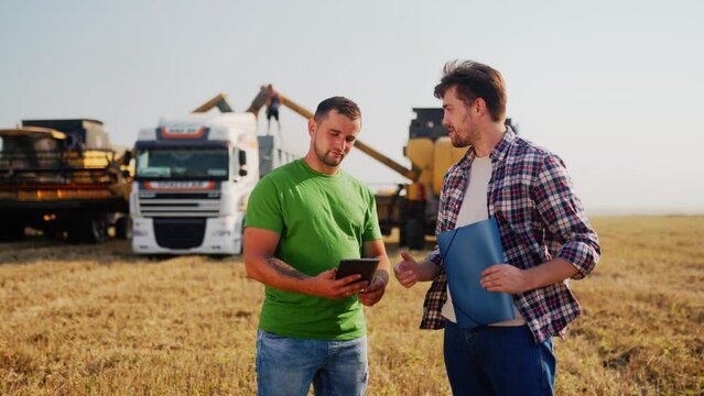 Farmer and agronomist shaking hands in wheat field after agreement. Agriculture business contract concept. Corporate farmer and landlord rancher negotiate with handshake. Combine harvesters harvest.