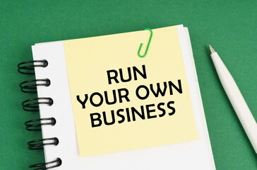 On a green surface, a pen, a notepad with stickers and the inscription - Run Your Own Business