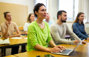 Asian woman studying with group of students in university, using laptop.