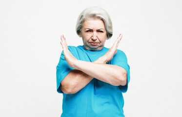 Stop. There is no way. Portrait of serious elderly woman in blue tshirt standing with X sign and looking at camera.