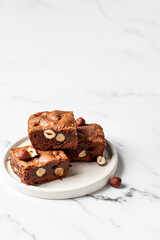 Brownies with nuts on white plate on marble background close up, homemade dessert, copy space