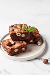 Brownies with nuts and mint leaf on white plate on marble background close up, homemade dessert