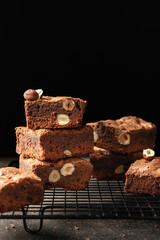 Chocolate brownies with nuts stacked on baking rack on dark background, text space