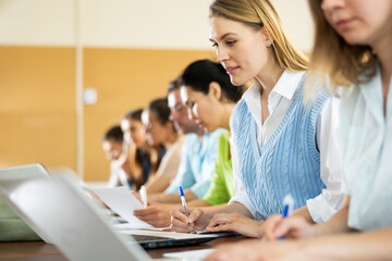 Woman university student sitting at table in classroom and writing. University students sitting in a row.