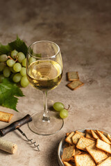 A glass of white wine on textured background with corkscrew and grapes and crackers. Text space