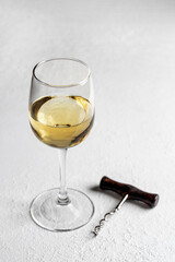A glass of white wine on white textured background with corkscrew. Copy space