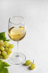 A glass of white wine on white textured background with grapes with text space
