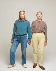 Two happy elderly women friends on grey background. Full length portrait.