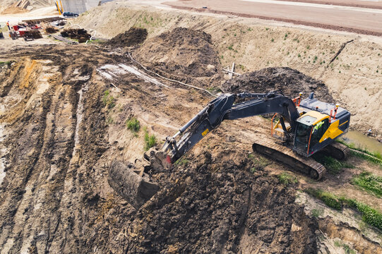 Dark-colored industrial machine with a giant shovel digging in sand. Road construction site, drone shot. High quality photo