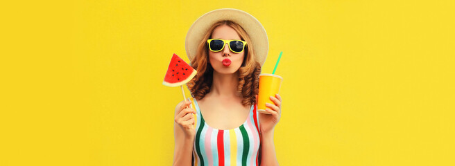 Summer colorful portrait of beautiful young woman blowing her lips with cup of juice and lollipop or ice cream shaped slice of watermelon wearing straw hat on yellow background, blank copy space - obrazy, fototapety, plakaty