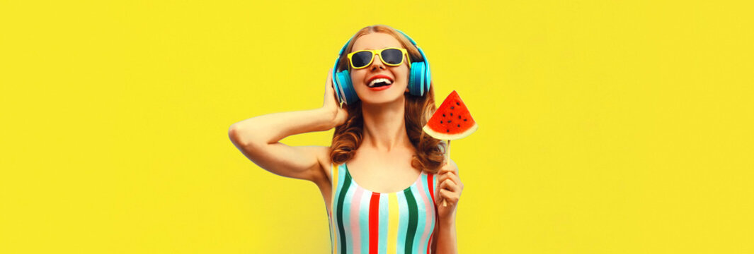 Summer colorful portrait of cheerful happy laughing young woman in headphones listening to music with juicy lollipop or ice cream shaped slice of watermelon on yellow background
