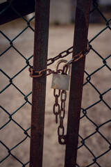 Close-up of a locked rusty old gate tethered by a chain and padlock with blurred background. Image in brown tones with vertical orientation