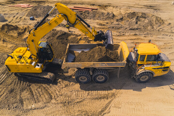 A yellow huge digger loading sand onto a long tipper truck. Works at a road construction site....