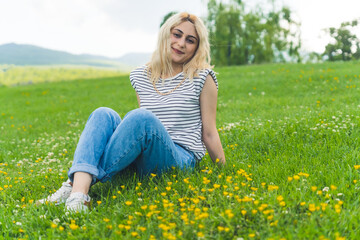 Fototapeta premium cute blond Caucasian girl on the grass smiling at the camera. park background full shot summer concept. High quality photo