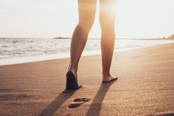 Beach travel - woman walking on sand beach leaving footprints in the sand. Closeup detail of female...