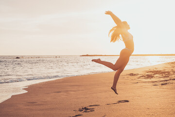 One happy and healthy young woman jumping on the sand of the beach having fun and enjoying summer outdoors. Beautiful attractive girl playing.