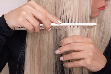 
Young beautiful woman brushing her long healthy blonde hair in hairdressing salon

