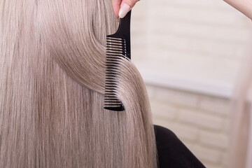 Naklejka premium Hairdresser's hand brushing long silver blonde hair in beauty salon 