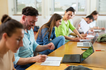 Portrait of a student guy with fellow students, studying on a laptop and writing a synopsis lecture...