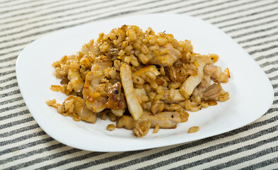 Close up of tasty barley groats with frying pork at plate on table
