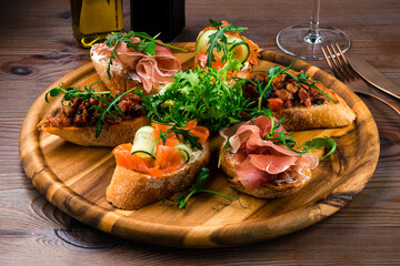 Brushetta set for wine. Variety of small sandwiches with prosciutto, parmesan cheese served on rustic wooden board