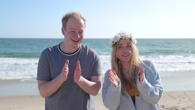 Portrait of a man and a woman enjoying sunny summer day with beautiful seascape around. Lovely couple clapping with their hands at sandy beach. High quality 4k footage
