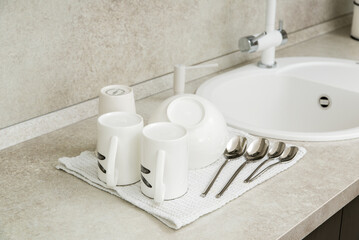 Cups and spoons dry on a towel next to the kitchen sink.