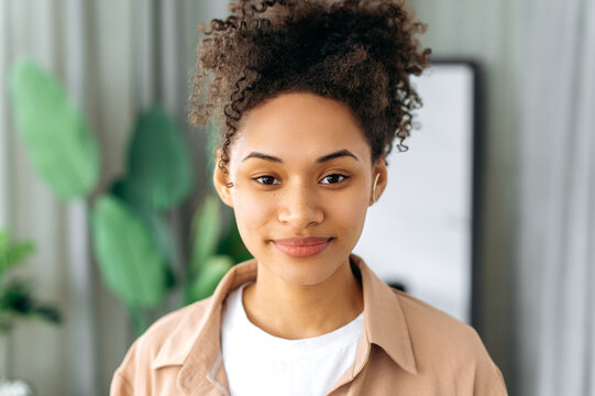 Portrait of a beautiful charming African American curly haired girl with freckles, dressed in a casual clothes, standing indoors, looking directly at the camera with a slight smile