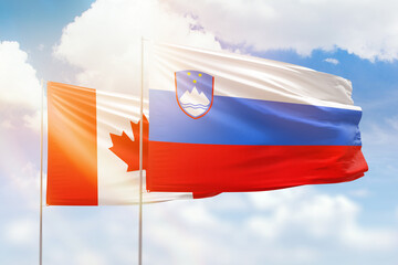Sunny blue sky and flags of slovenia and canada