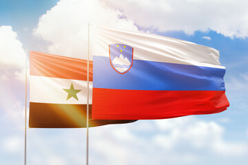 Sunny blue sky and flags of slovenia and syria