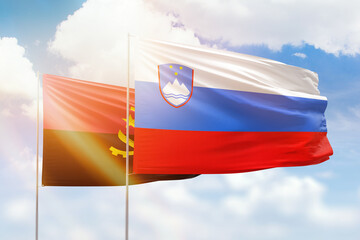 Sunny blue sky and flags of slovenia and angola