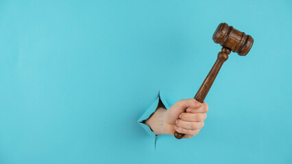 A woman's hand with a wooden judge's gavel sticks out of a hole in a blue background. Copy space. 