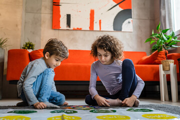 Brother and sister siblings small caucasian boy and girl child play twister game on the floor at home alone real people family growing up leisure concept copy space