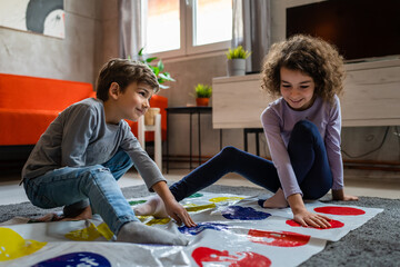 Brother and sister siblings small caucasian boy and girl child play twister game on the floor at...