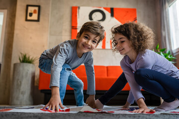 Brother and sister siblings small caucasian boy and girl child play twister game on the floor at...