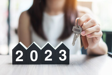 Businesswoman hands holding key and 2023 Happy New Year with house model on table office. New House, Financial, Property insurance, real estate, savings and New Year Resolution concepts