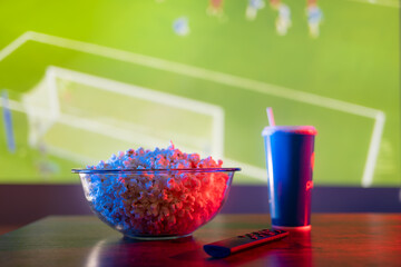 A football match on the big TV screen. Popcorn, a carbonated drink in a plastic glass and a TV...