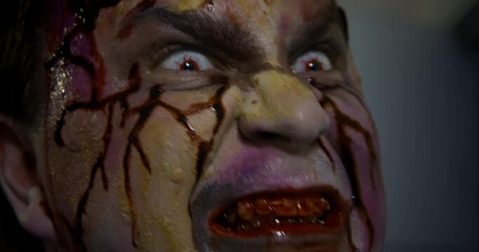 Portrait of an enraged hungry male zombie who sees the prey and wants to attack, so he clicks his bloody teeth with braces and disgustingly sticks out his tongue, close up