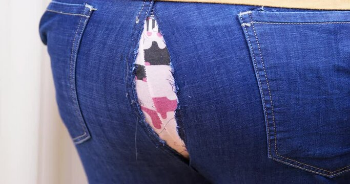 Plump man touches back of jeans coming apart at seam with hand standing against white wall. Guy finds out about big torn hole on pants closeup