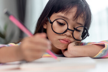 Fototapeta na wymiar Little Asian girl sitting alone and looking out with a bored face, Preschool child laying head down on the table with sad bored with homework, spoiled child