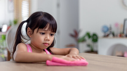 happy little Asian girl learning to clean with a rag in the living room at home. housework and household concept.