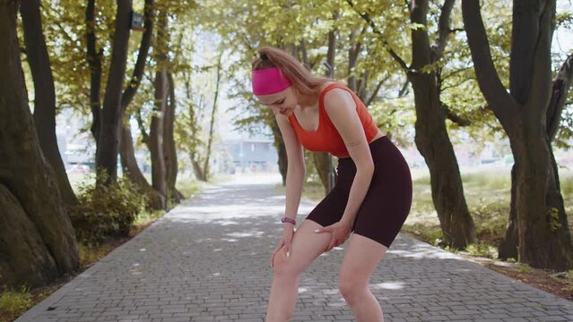 Athletic fit runner girl with muscle pain. Young woman massaging stretching, trauma injury while jogging outdoors in park. Fitness female sprain severe pain stretch pull. Leg muscle cramp calf sport
