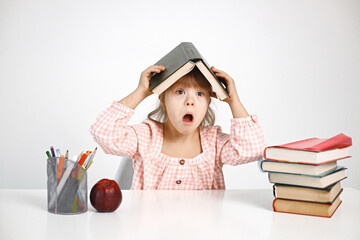 Girl with Down syndrome sitting at desk and holding a book on her head