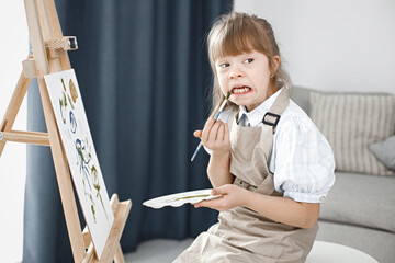 Girl with Down syndrome wearing beige apron and painting on an easel