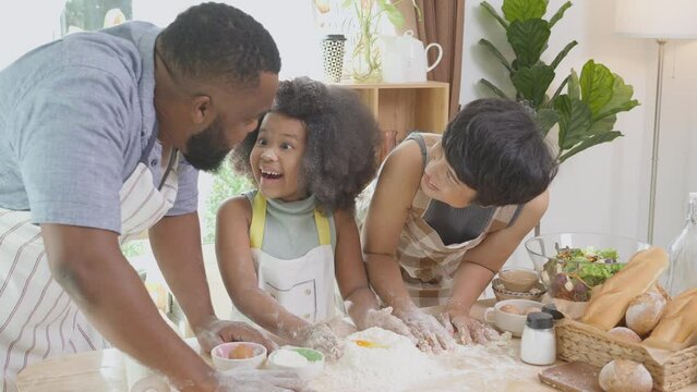 African American family with daughter thresh flour with excited for cooking with father and mother together in the kitchen at home, parent and little child activity preparing food with fun.
