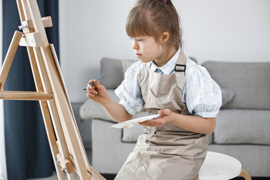 Girl with Down syndrome wearing beige apron painting on an easel