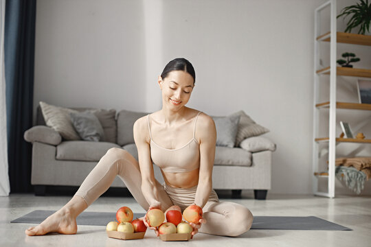 Young fitness woman sitting on yoga mat at home and holding fresh apples