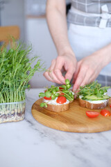 Woman preparing healthy sandwiches with microgreens and vegetables
