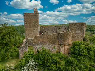 Close up aerial view of the rectangular keep, ruined Gothic palace and circular defensive tower at Brancion castle and medieval village in Central France with cloudy blue sky